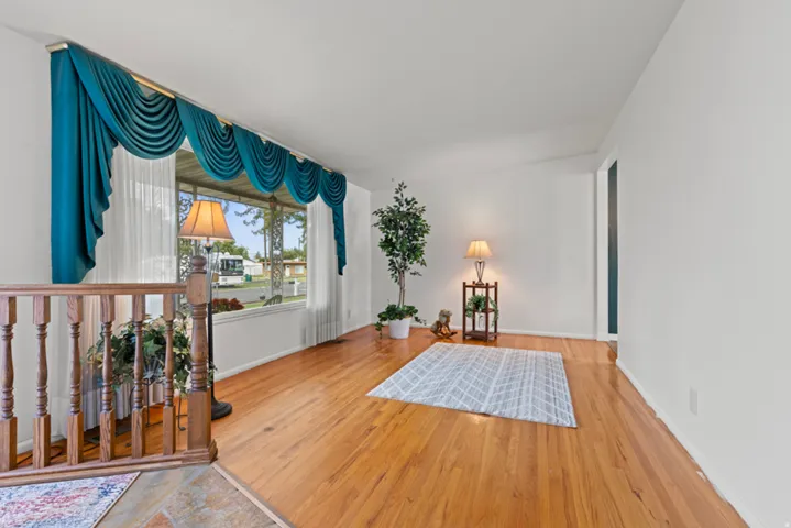 Hardwood flooring throughout the room, large picture window, white painted walls, and wood railing