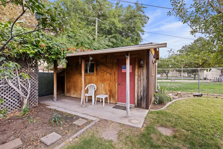 Wood-sided storage shed with a covered concrete patio, red door, and a single window