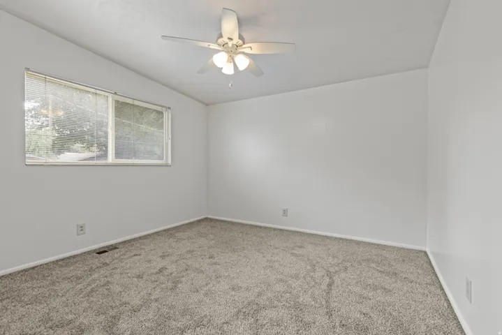 Gray carpeting with a neutral wall color, large window, and ceiling fan with integrated lighting