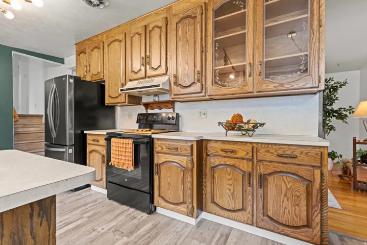Kitchen featuring wood-finish cabinetry, light-toned countertops, a black range, and wood-finish flooring
