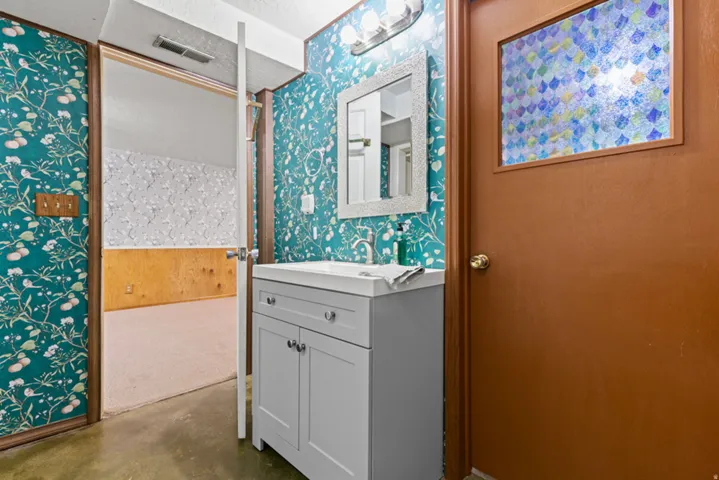 Bathroom vanity with a white countertop and basin, recessed cabinet doors, and polished chrome hardware