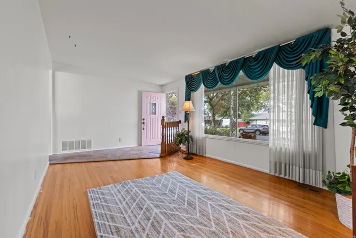 Hardwood flooring throughout the room, large picture window, white painted walls, and wood railing