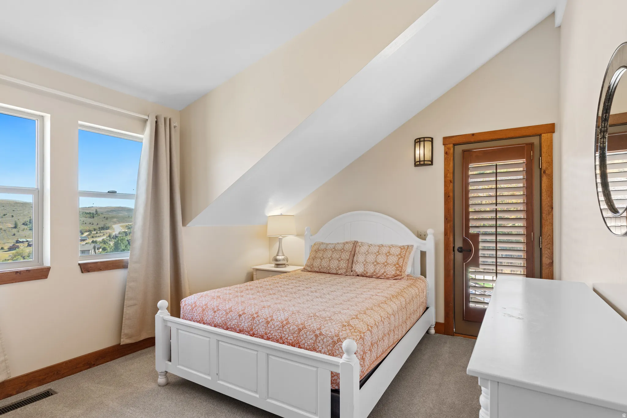 Sloped ceiling room featuring dual windows, wood-trimmed door with louvered shutters, wall-mounted sconce, and carpeted flooring
