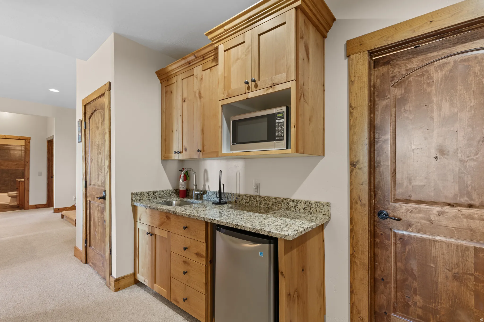 Built-in wet bar with wood cabinetry, granite-finish countertop, stainless steel sink, and compact refrigerator