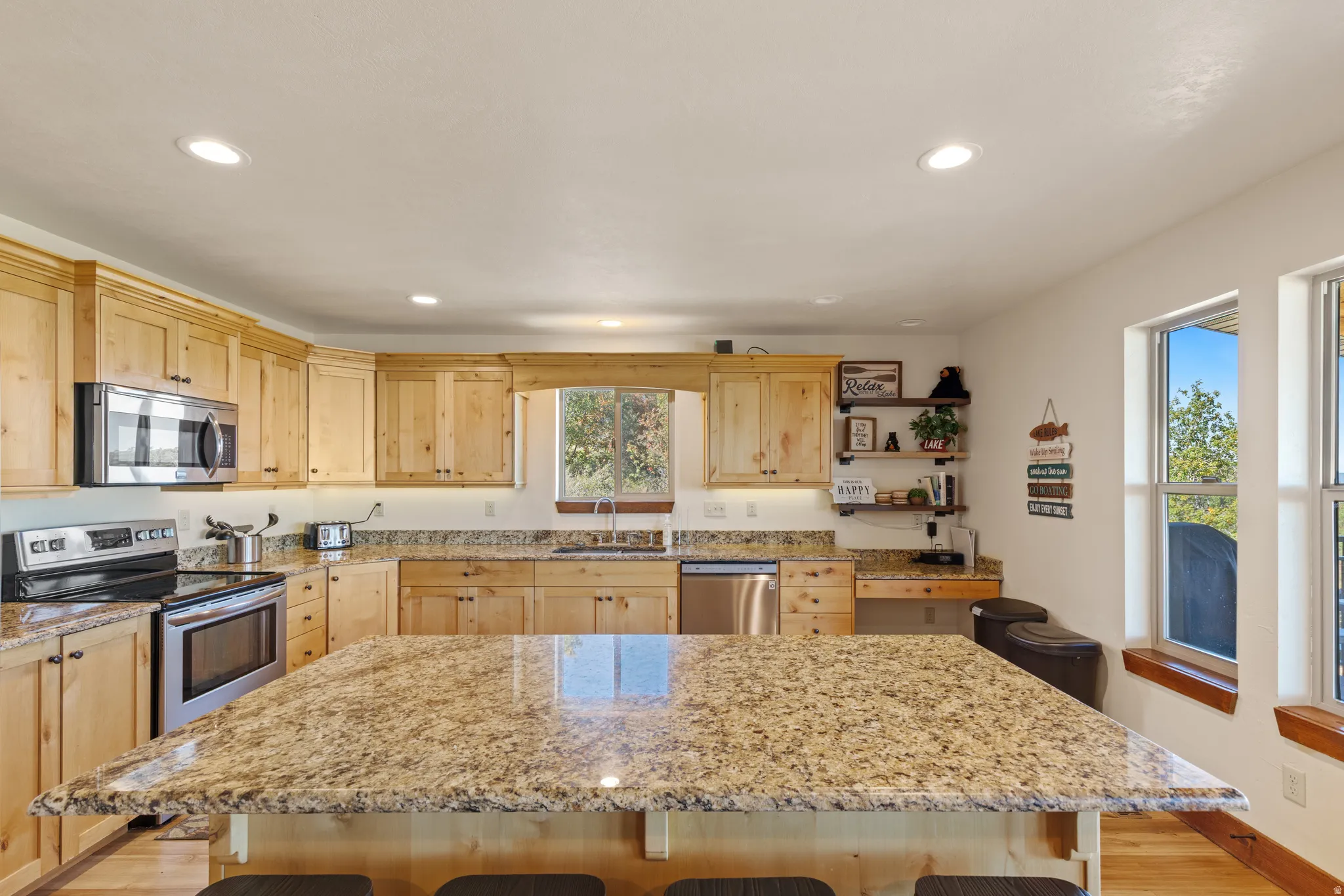 Expansive kitchen island with stone countertops, stainless steel appliances, extensive wood cabinetry, and recessed lighting