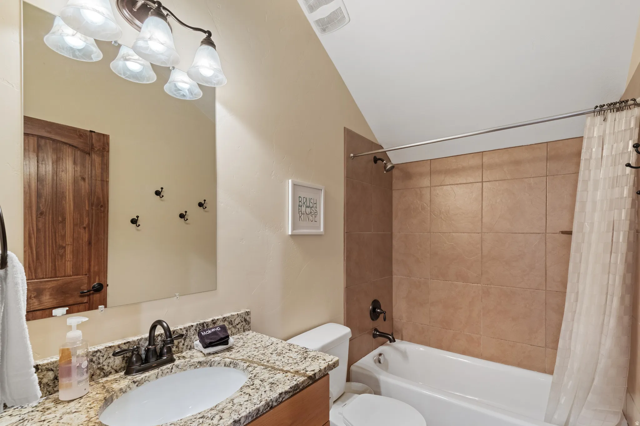 Bathroom featuring a tiled shower/tub combination, granite-style countertop, undermount sink, and wood-finish door