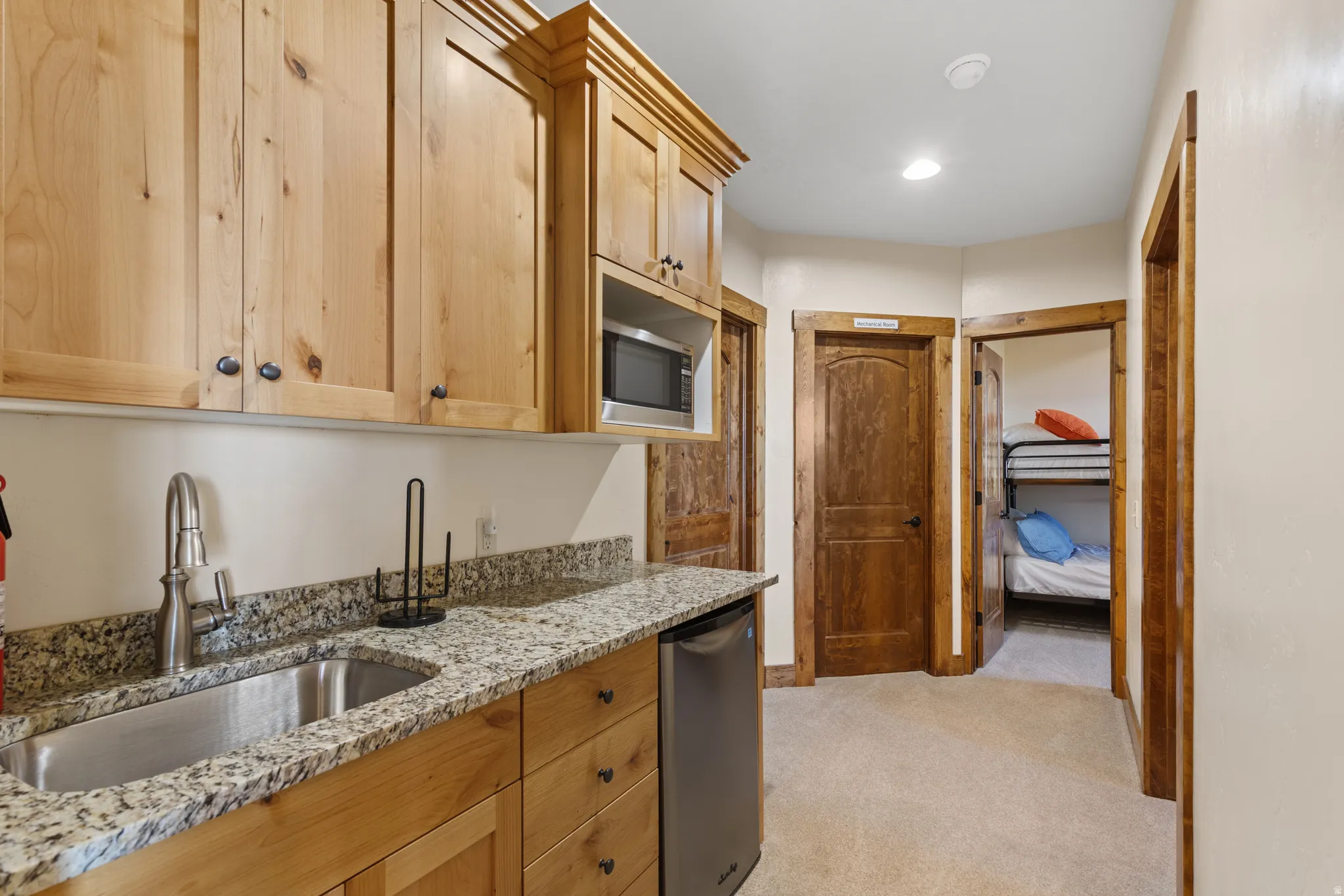 Built-in kitchenette featuring wood cabinetry, a stainless steel sink, and stone-finish countertops