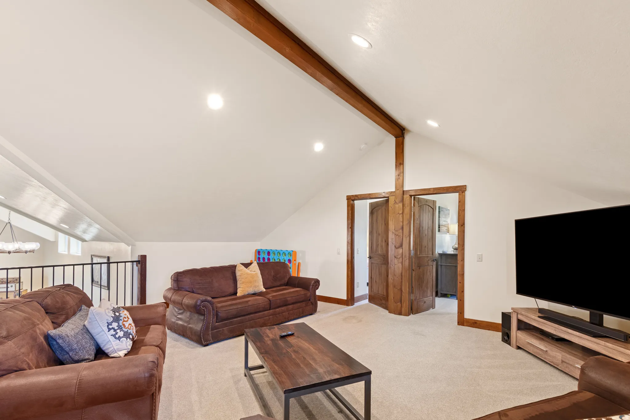 Vaulted ceiling with exposed wood beam, recessed lighting, and wood-paneled doors