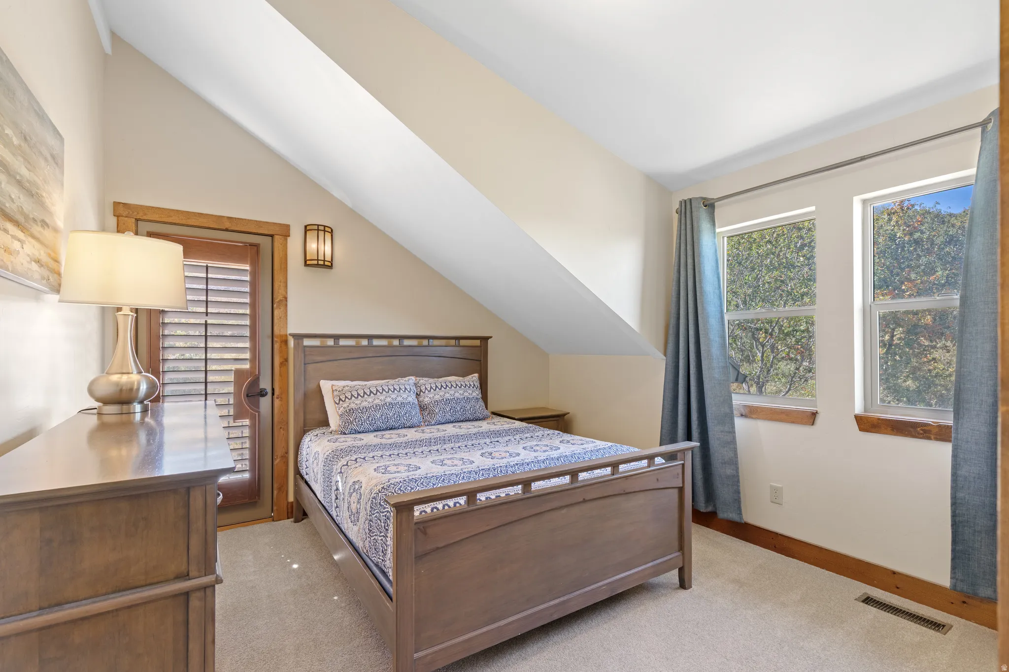 Carpeted room featuring a sloped ceiling, wood-trimmed windows, a wood-trimmed exterior door with louvered blinds, and a wall-mounted light fixture