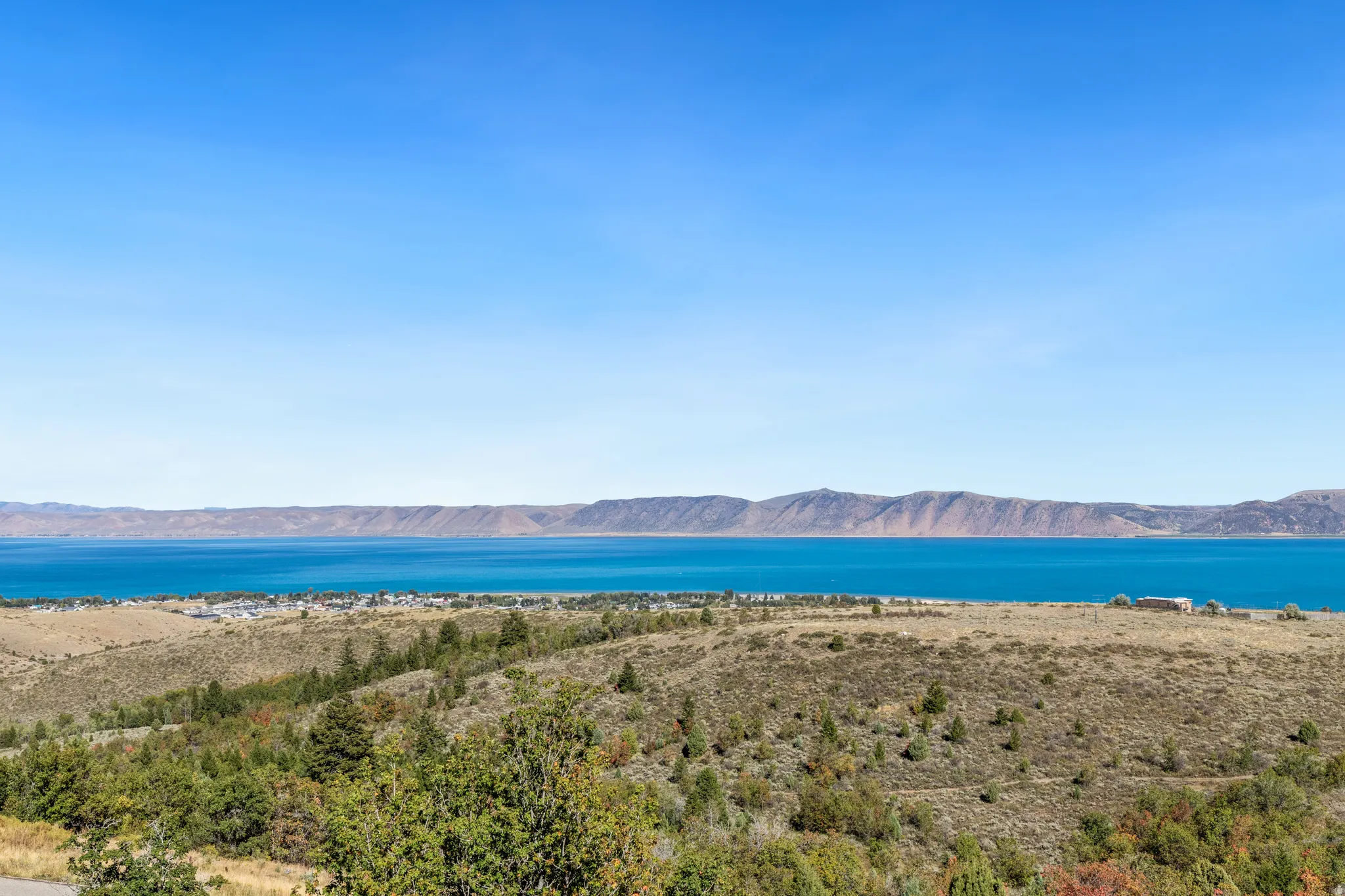 Expansive water body, mountainous terrain, and distant developed land under a clear sky
