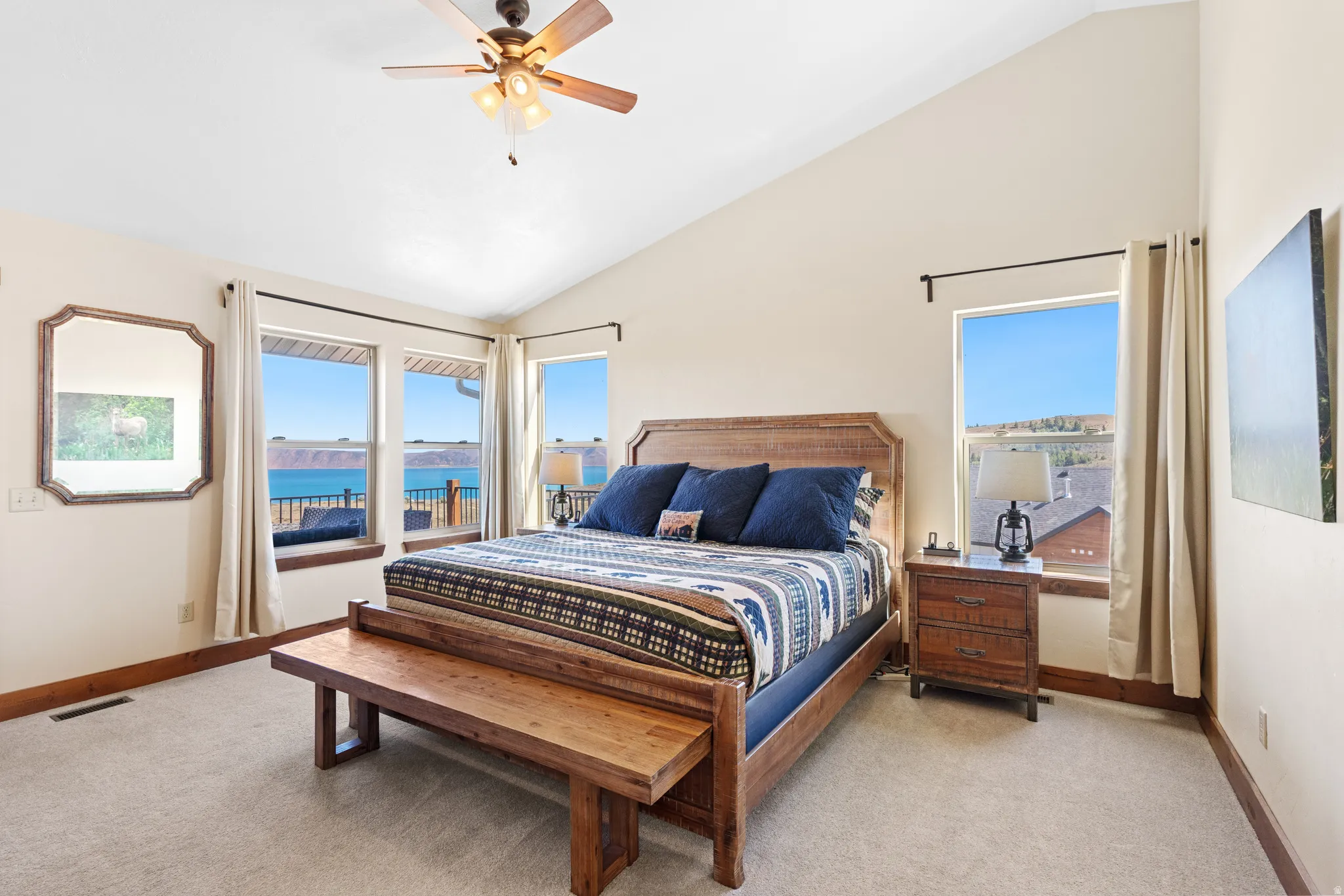 Vaulted ceiling bedroom with carpeting, ceiling fan, and multiple windows offering water scenery