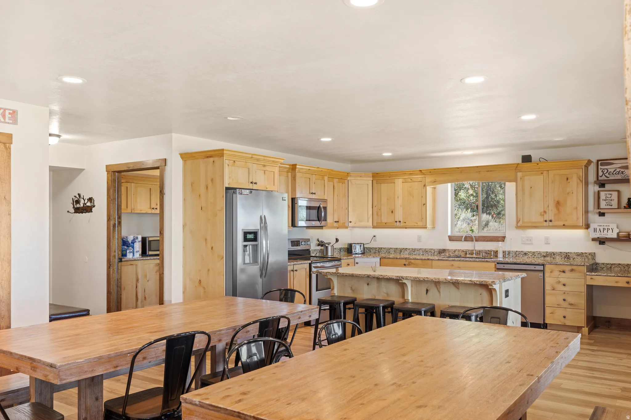 Kitchen featuring wood-finish cabinetry, stainless steel appliances, a large center island with seating, stone countertops, and recessed lighting