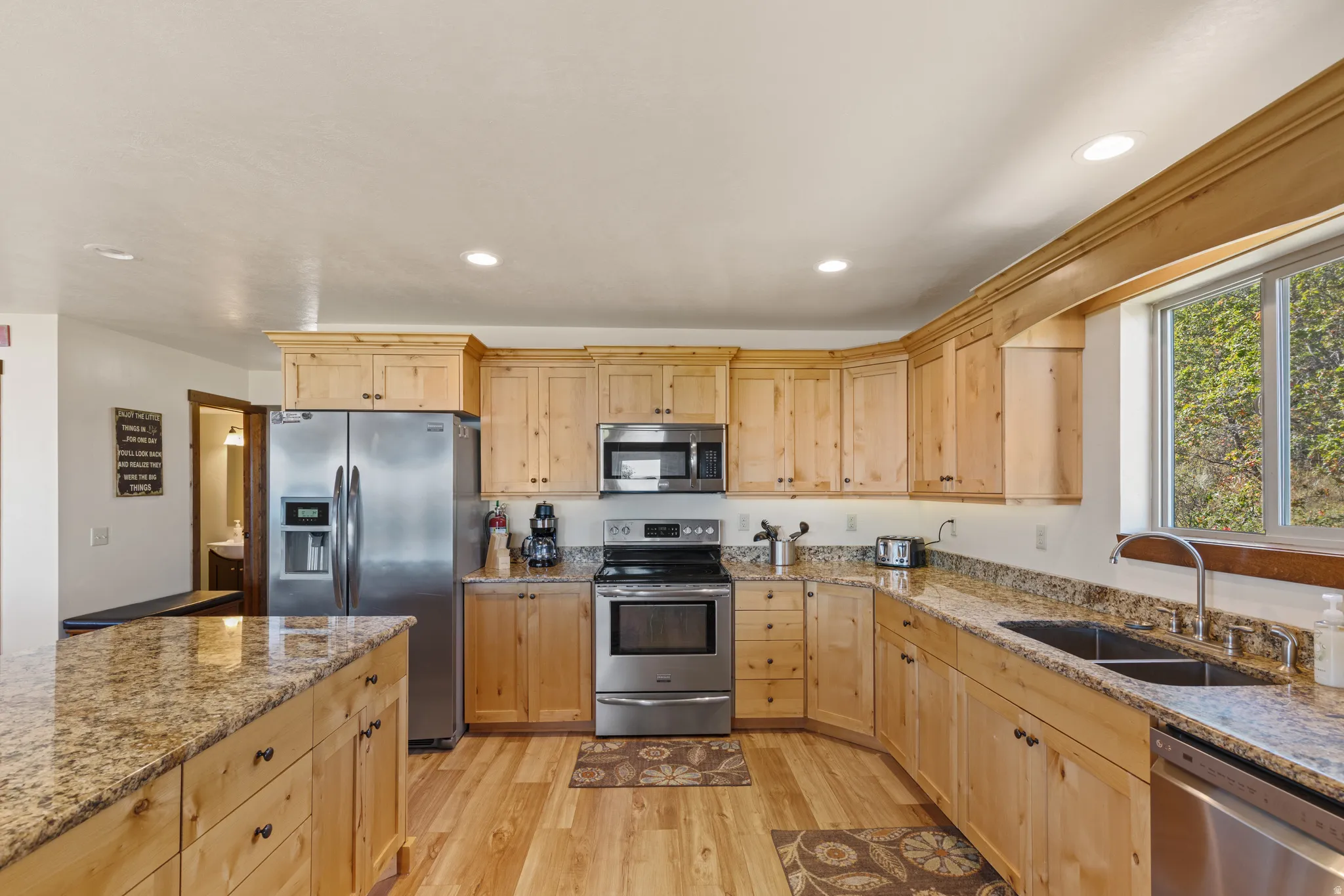 Stainless steel appliances, recessed ceiling lighting, light wood-finish cabinetry, granite countertops, and wood-finish flooring