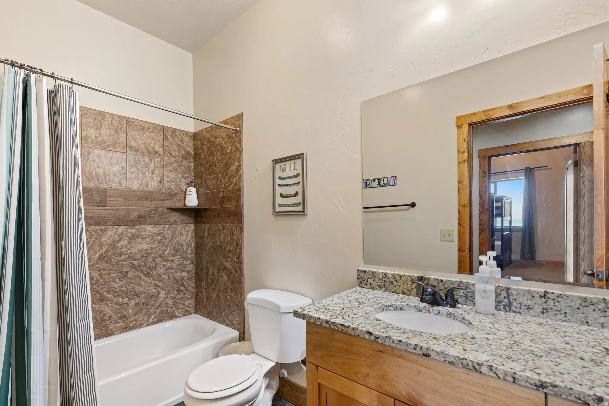 Bathroom featuring a full-size bathtub, tiled shower surround with an integrated shelf, wood-finish vanity, granite countertop, and a framed mirror