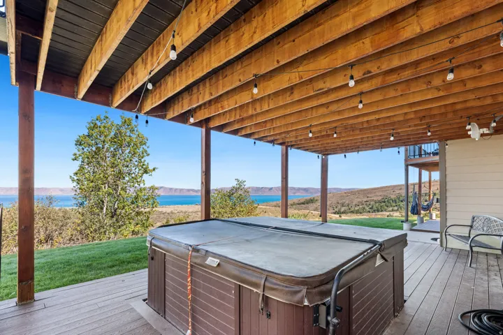 Expansive outdoor deck with a built-in spa, overhead string lighting, and distant water scenery