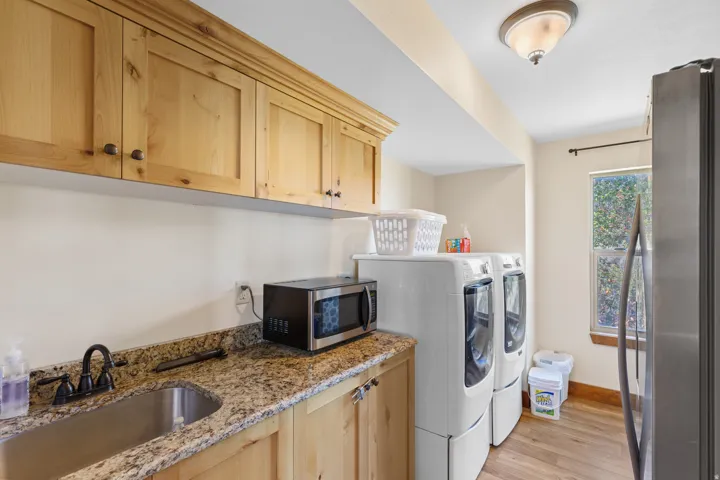 Built-in wood cabinetry, granite-style countertop, stainless steel sink, wood-finish flooring, and a single window