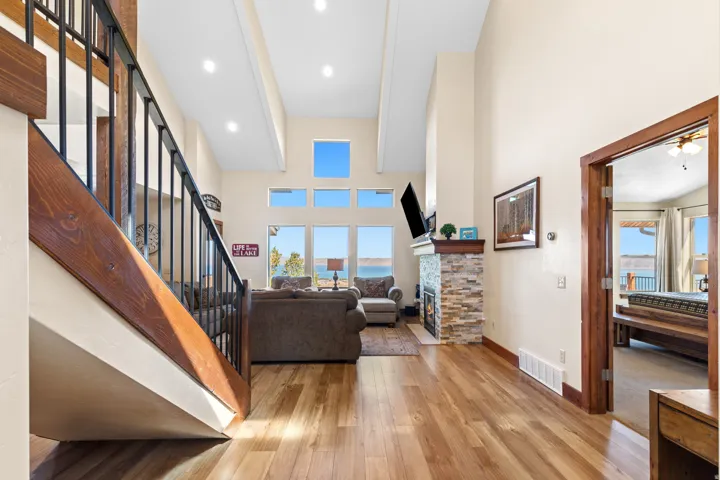 Vaulted ceiling with recessed lighting, wood-finish flooring, stacked stone fireplace, large picture windows, and a wood-trimmed doorway