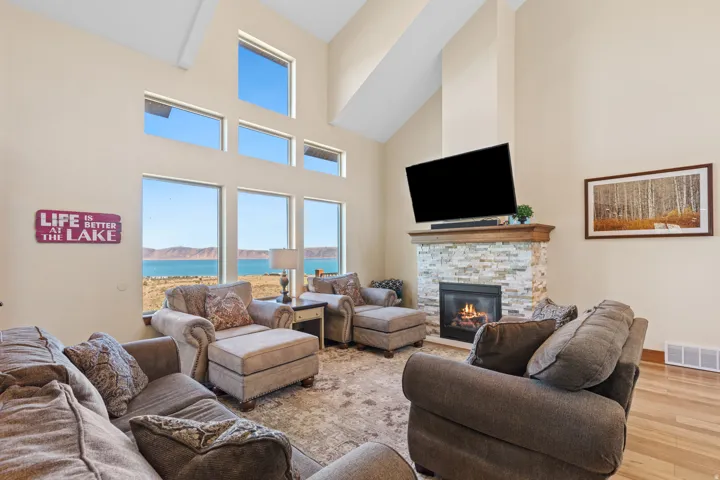 Vaulted ceiling with high windows, stone-clad fireplace with mantel, and hardwood flooring