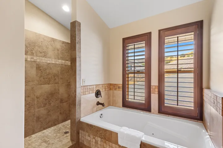 Built-in tub with dark bronze fixtures, framed by two windows with dark wood shutters