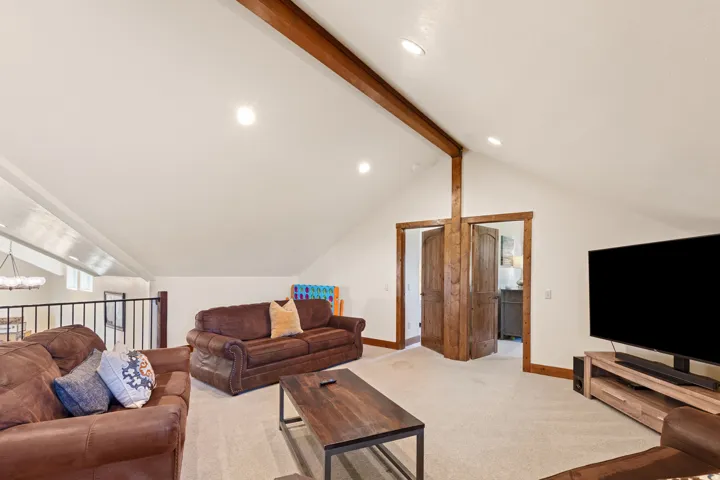 Vaulted ceiling with exposed wood beam, recessed lighting, and wood-paneled doors