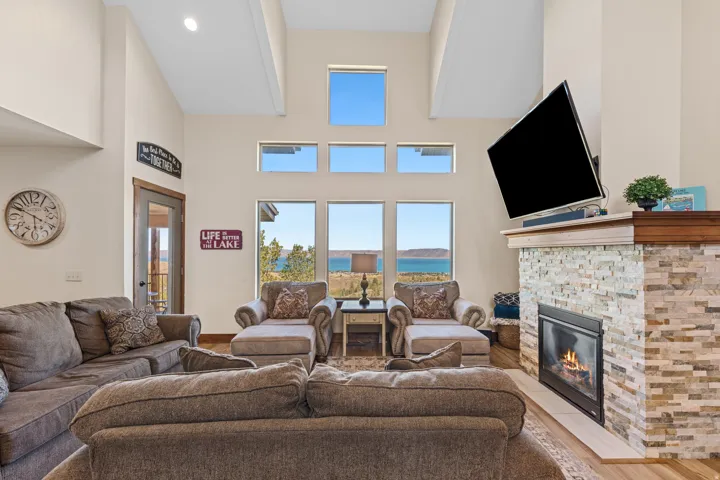 Vaulted ceiling with exposed beams, stone-clad fireplace, built-in fireplace, large windows, and a glass-paneled door