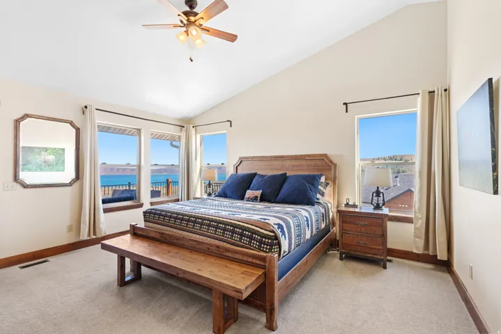 Vaulted ceiling bedroom with carpeting, ceiling fan, and multiple windows offering water scenery