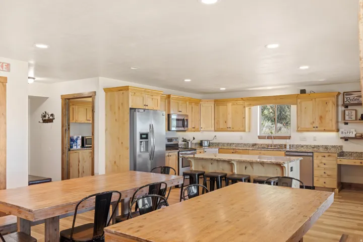 Kitchen featuring wood-finish cabinetry, stainless steel appliances, a large center island with seating, stone countertops, and recessed lighting