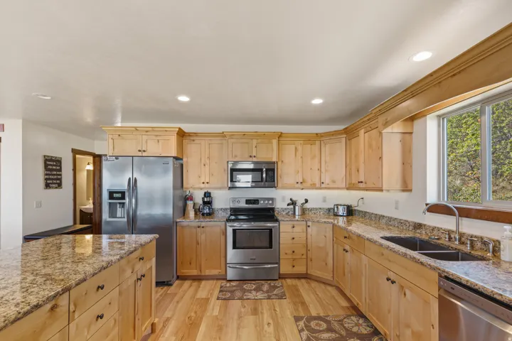 Stainless steel appliances, recessed ceiling lighting, light wood-finish cabinetry, granite countertops, and wood-finish flooring