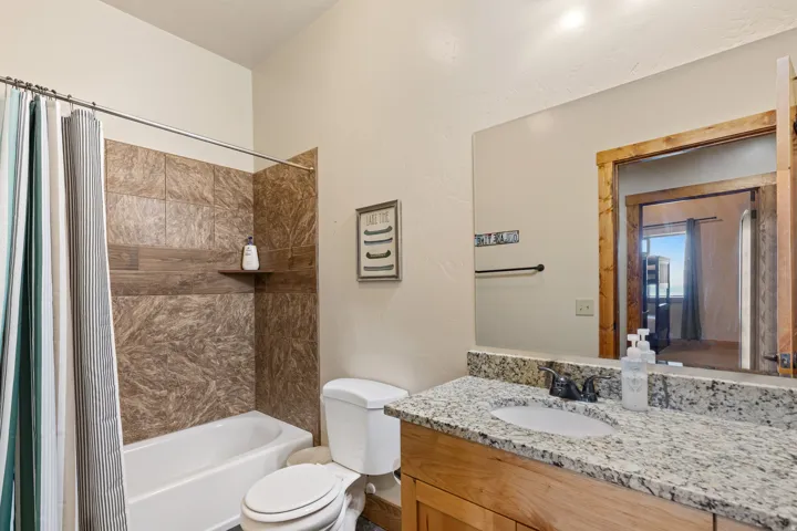 Bathroom featuring a full-size bathtub, tiled shower surround with an integrated shelf, wood-finish vanity, granite countertop, and a framed mirror