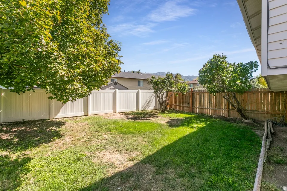 Expansive backyard featuring a combination of wood and vinyl fencing, mature trees, and a green lawn