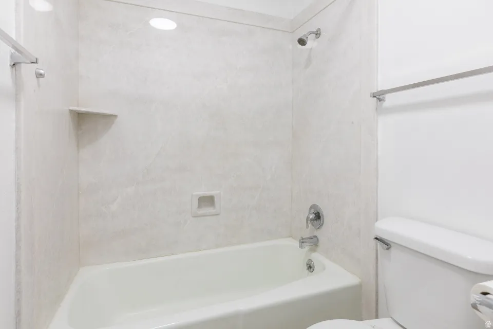 White bathtub with chrome fixtures, integrated wall shelving, and a toilet with chrome details