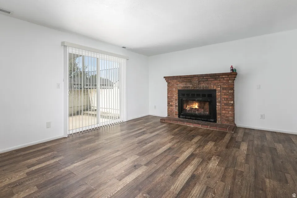 Brick fireplace with mantel and hearth, wood-finish flooring, and white walls