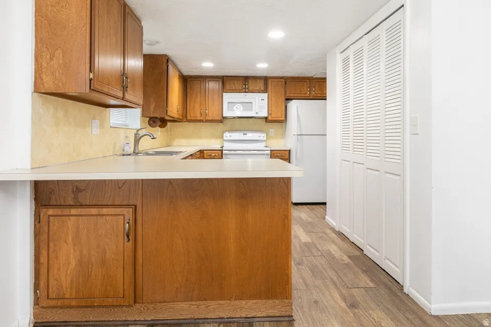 Kitchen featuring wood-finish cabinetry, white countertops, built-in microwave, white refrigerator, and wood-finish flooring
