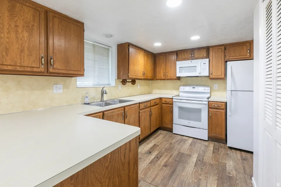 Kitchen featuring wood-finish cabinetry, light countertops, wood-finish flooring, and white appliances