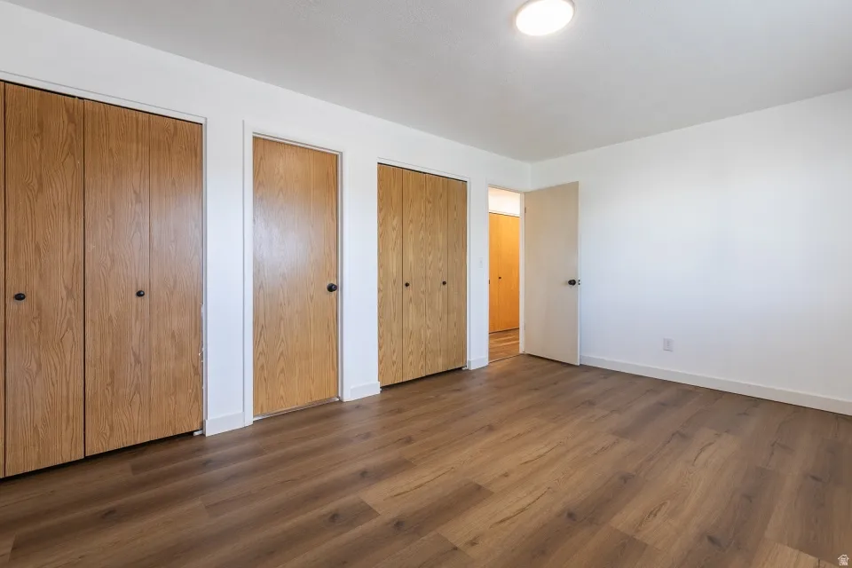 Wood-finish flooring, multiple bi-fold closet doors, standard door with round knob, white walls, and a ceiling-mounted light fixture