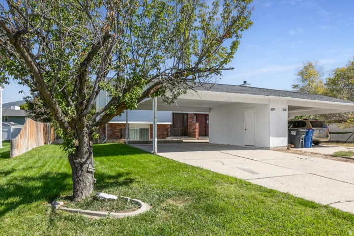 Expansive carport with integrated storage unit, a paved driveway, and established front landscaping