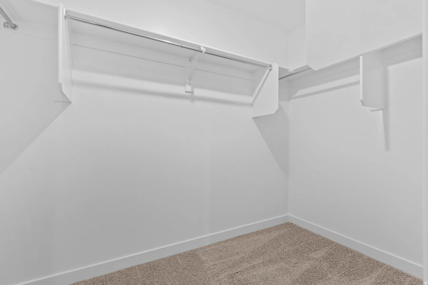 Carpeted closet with white shelving and chrome hanging rods