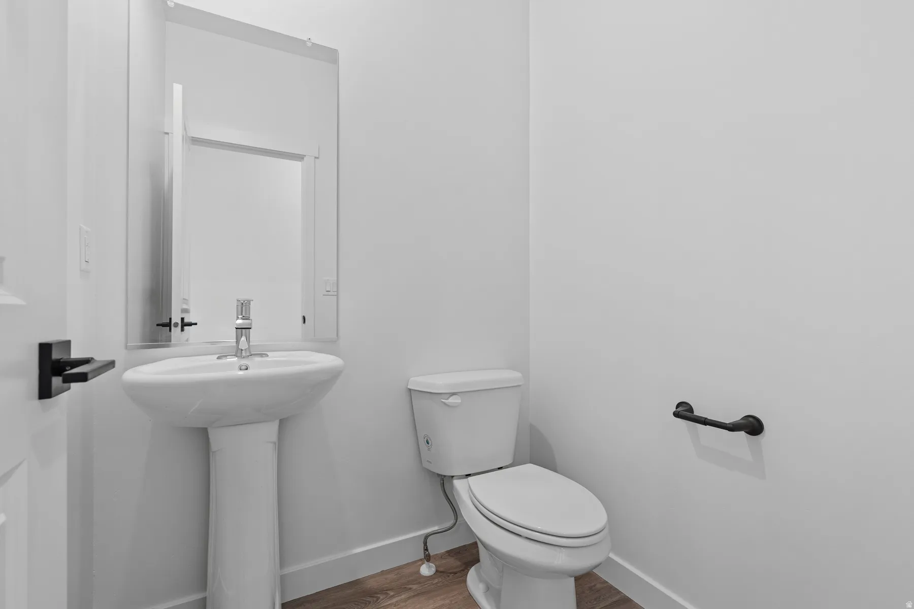 Pedestal sink with chrome faucet, wall-mounted rectangular mirror, white toilet, and wood-finish flooring