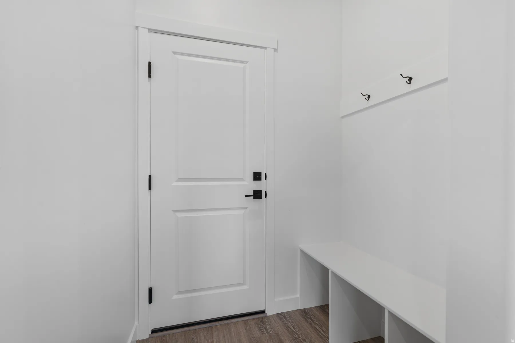 White interior door with matte black hardware, wood-finish flooring, built-in coat hooks, and integrated bench seating