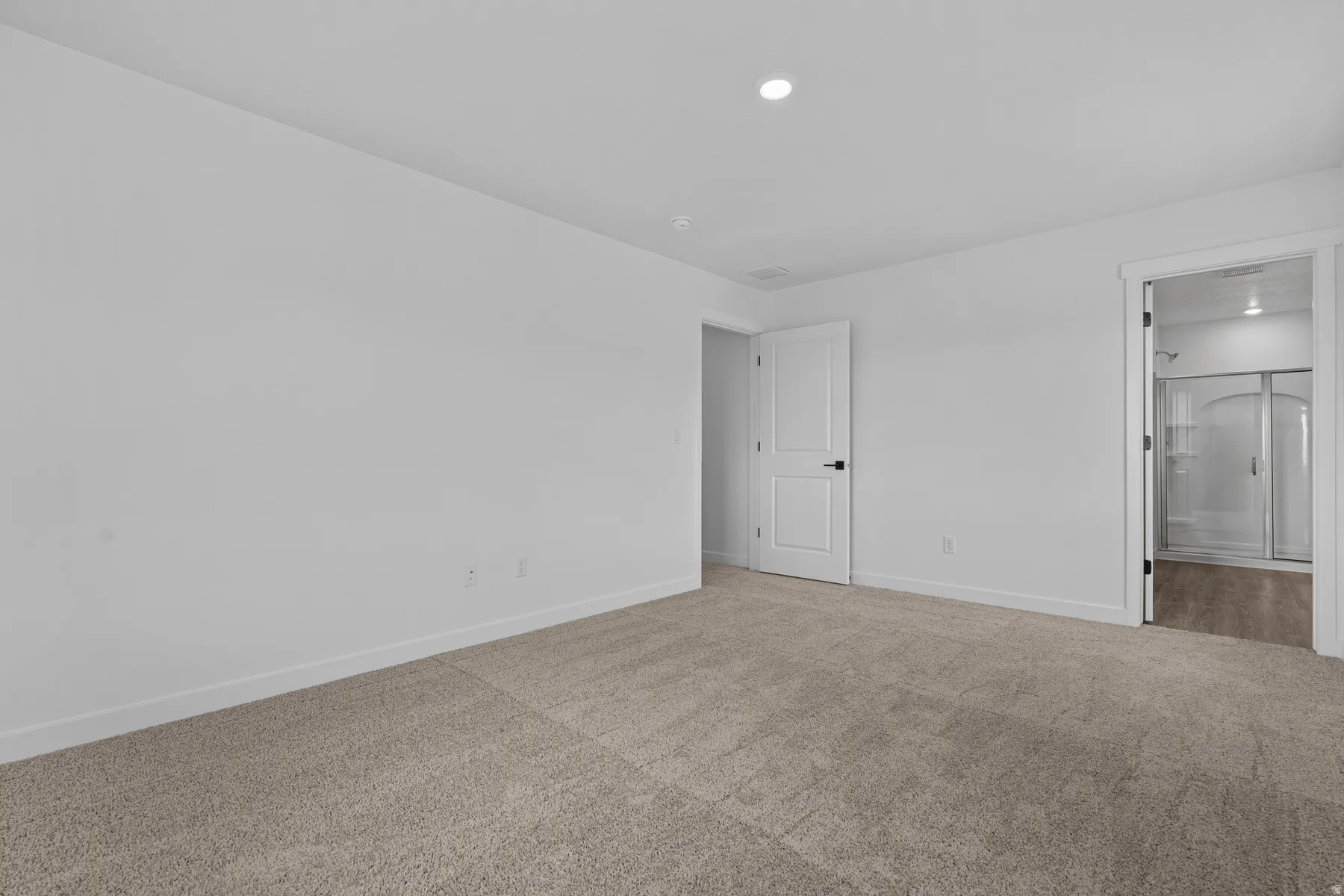 Recessed ceiling lighting, white walls, light-colored carpet, white interior door with black hardware, and a framed doorway