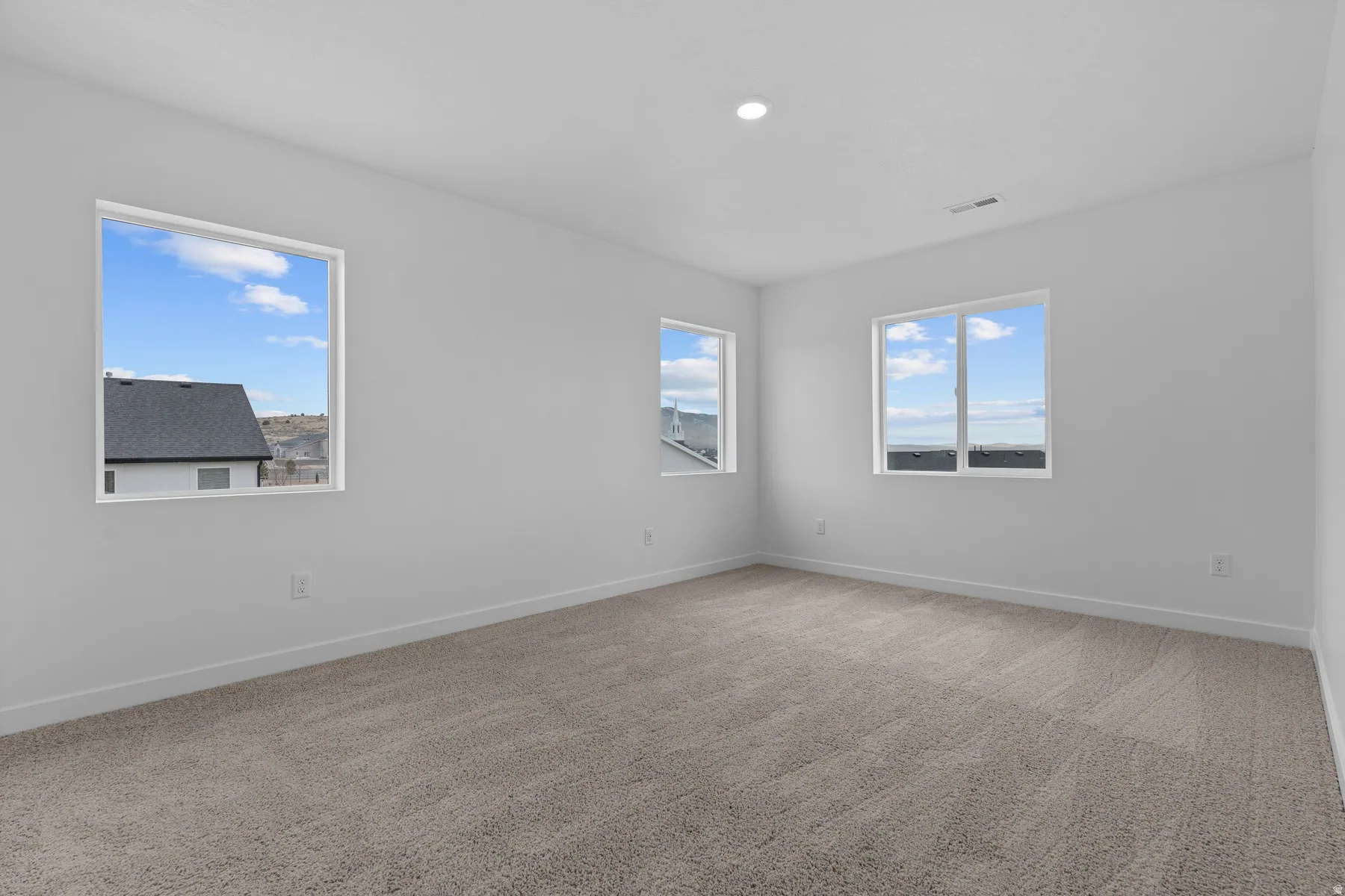 Neutral-toned carpeting, white walls, and multiple windows providing ambient light