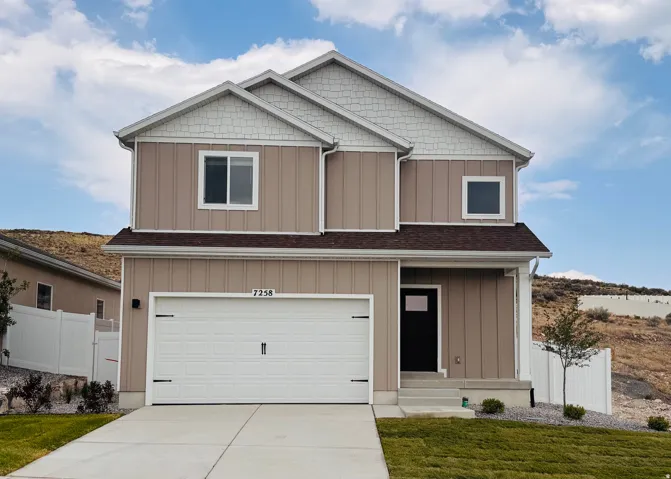 Two-story residence featuring vertical siding, white garage door, dark entry door, concrete driveway, and a partially fenced yard