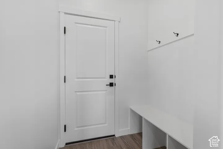 White interior door with matte black hardware, wood-finish flooring, built-in coat hooks, and integrated bench seating
