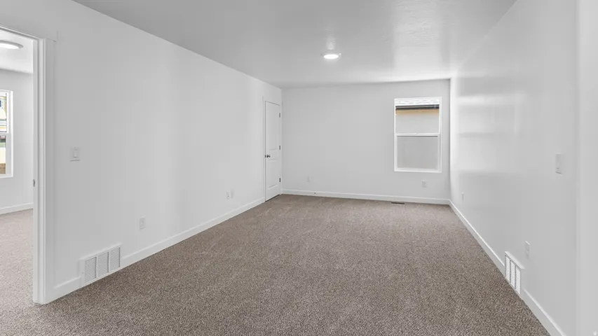 Neutral tone carpeting, white painted walls, recessed lighting, white trim, and a window providing natural illumination