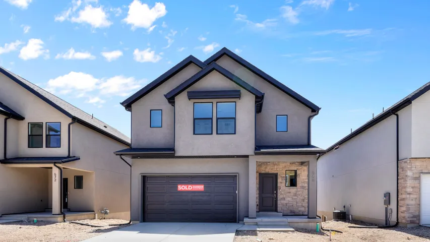 Contemporary stucco exterior with a dark-framed garage door, stone veneer accents, and dark trim details