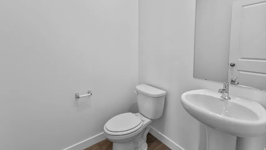 White pedestal sink with chrome faucet, toilet with white lid, and wood-finish flooring