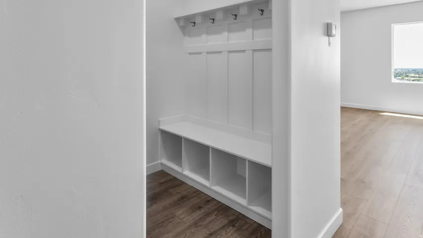Built-in white storage bench with cubbies, upper hooks, and wood-finish flooring
