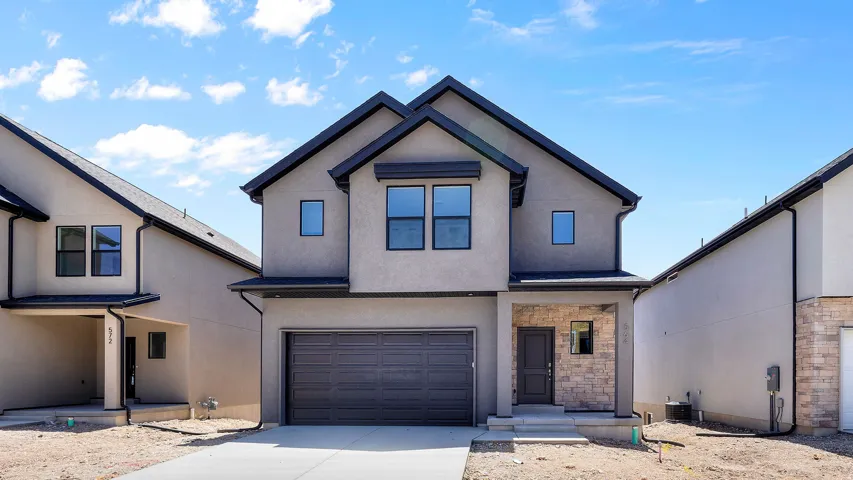 Contemporary exterior featuring a two-car garage, stone accents, dark trim, and a covered entryway