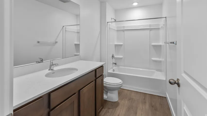 Wood-finish flooring, dark wood cabinetry, white countertop, integrated sink, and a white shower/tub combination