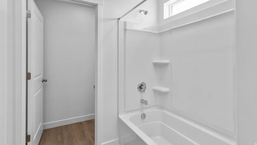 Bathtub with integrated shower surround, chrome fixtures, and upper transom window